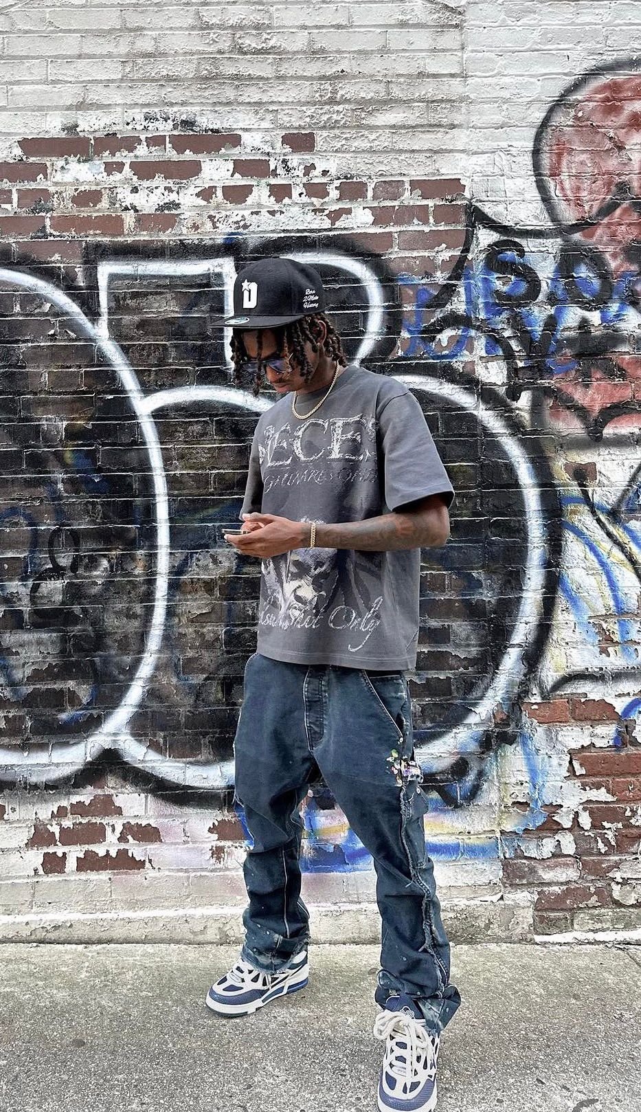 Pieces graphic tee in front of a graffiti brick wall